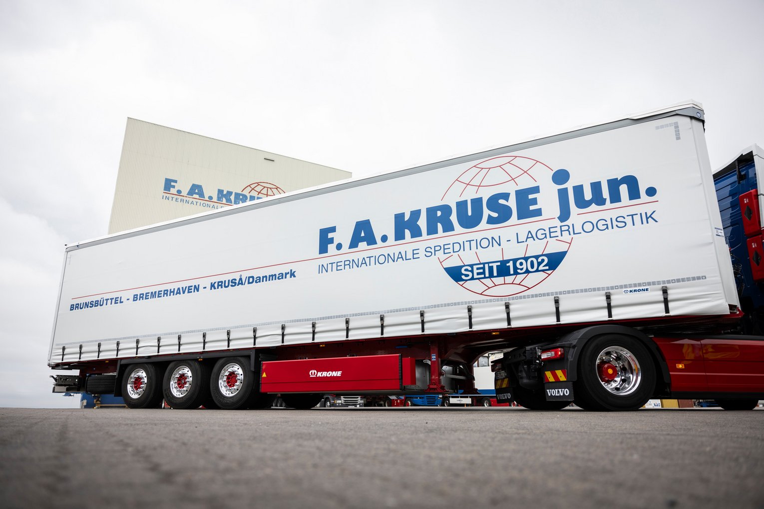 Sattelzug mit weißem Auflieger und F.A. Kruse jun.-Logo steht vor einer Lagerhalle.