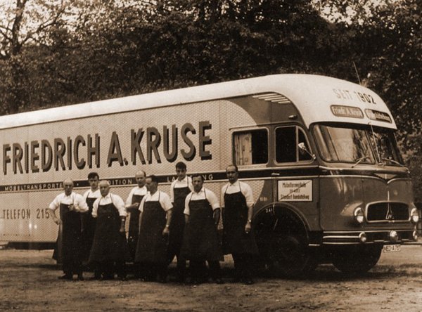 Historischer Lkw von Friedrich A. Kruse mit großem Schriftzug, davor stehen Mitarbeiter in Uniform.