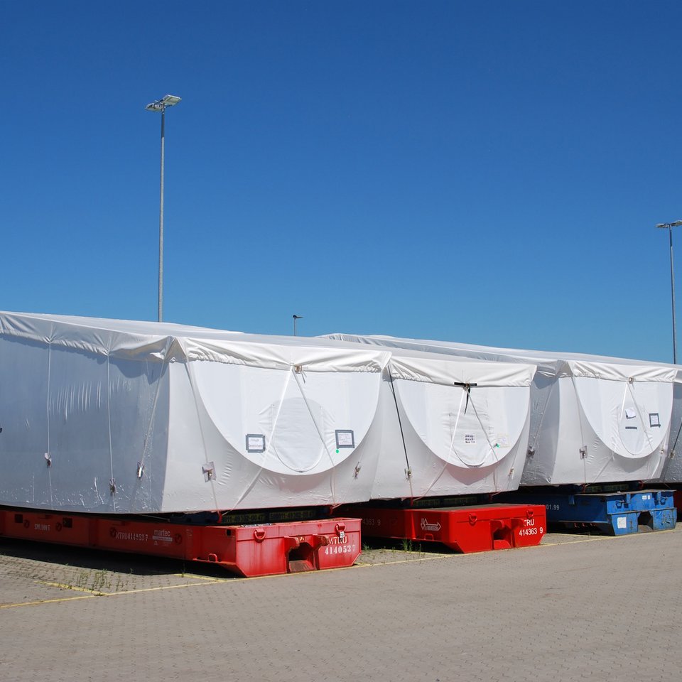 Verpackte Großkomponenten auf roten Transportplattformen im Außenlager unter blauem Himmel