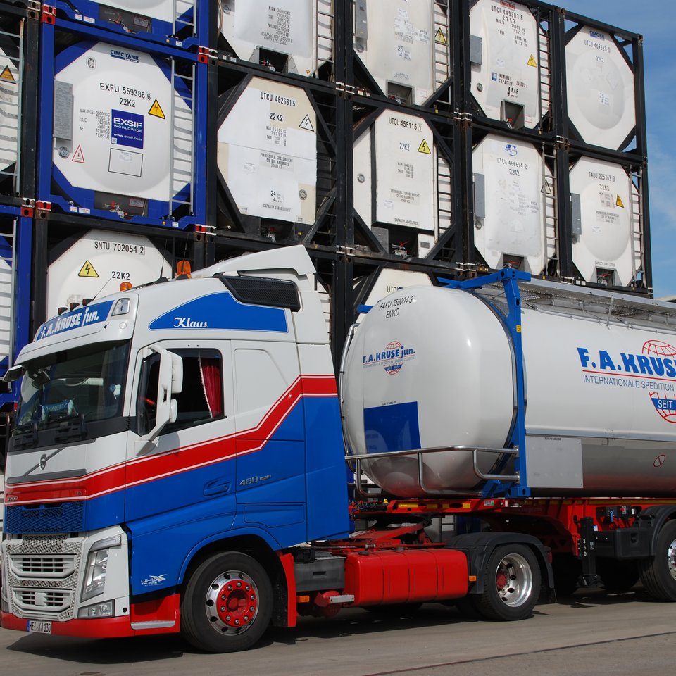 Lkw der Spedition Kruse mit Tankcontainer, im Hintergrund gestapelte Container mit Kruse-Logo